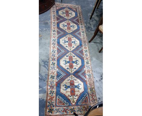Eastern runner with five cream ground central medallions, on a blue ground with red and cream diamond-shaped hooked motifs, t