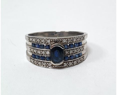 9ct white gold band ring set with a central oval mixed cut sapphire, surmounting three rows of grain set diamonds alternating