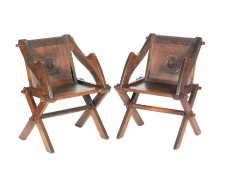 A pair of late 19th to early 20th Century oak Glastonbury chairs in the Gothic Revival style, with lozenge and relief carved 