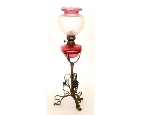 A Victorian oil lamp with ruby reservoir and shade on a brass open work tripod stand, height 61cm
