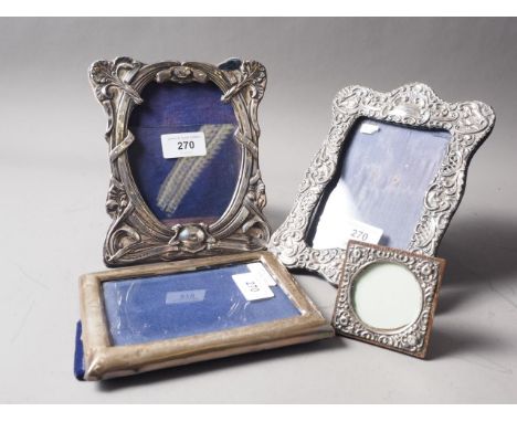A silver photograph frame with embossed scrolled decoration, another similar, and two others 