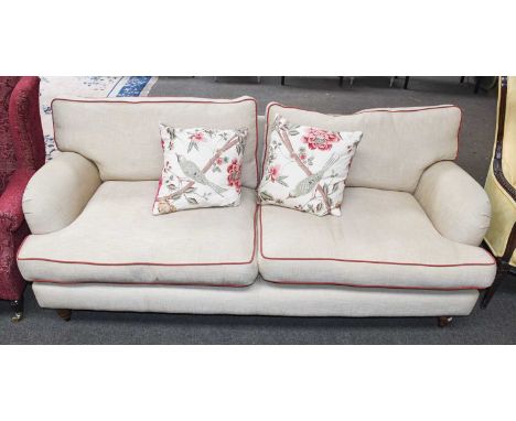 A Modern Two Seater Sofa, in beige upholstery with red piping, on turned wooden supports and with scatter cushions, 206cm by 