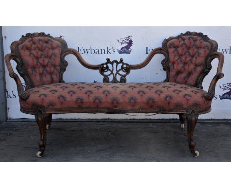 A Victorian walnut button back sofa, with foliate scroll carved back rests, sweeping arms, on cabriole legs, with ceramic cas