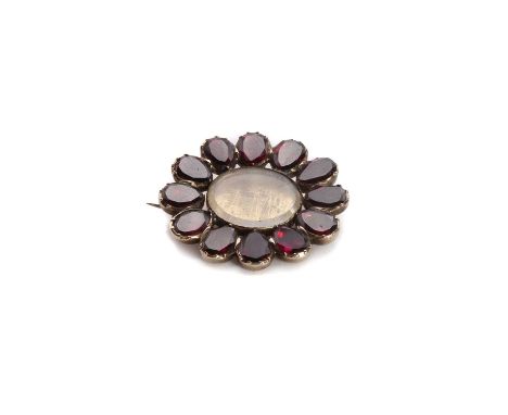 A Georgian gold garnet memorial brooch,an oval glazed panel to a surround of flat cut pear shape garnets, grain set to a plai