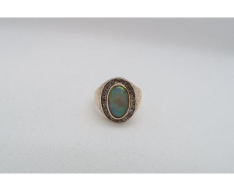 A 9ct yellow gold (hallmarked) opal and diamond ring - the central oval shaped opal approx 12mm x 7mm with diamond halo - rin