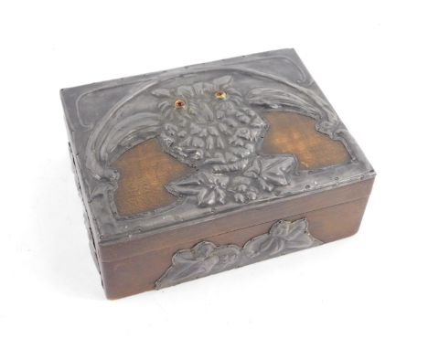 An early 20thC wooden cigarette box, mounted with arts and crafts hammered pewter design of an owl, with enamel eyes, in the 