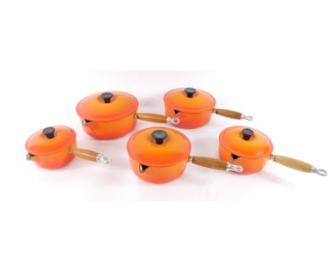 A set of five Le Crueset orange enamel graduated saucepans, with lids, and turned wooden handles, stamped TECK.