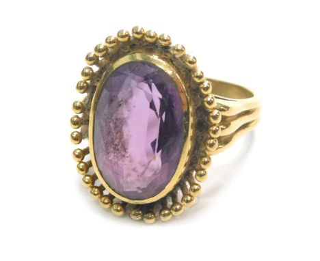 An 18ct gold amethyst dress ring, the chunky oval amethyst, with petalated floral border, on three strand shoulders, ring siz