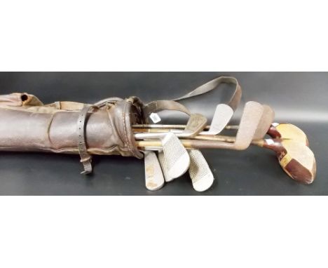 Vintage brown leather golf bag containing a collection of golf clubs, three hickory shafts, the others with steel shafts.