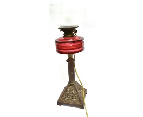 A VICTORIAN OIL LAMP  with cranberry glass reservoir, cast iron base and acid etched globe, 70cm high overall