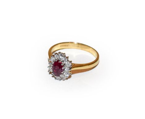 An 18 carat gold ruby and diamond cluster ring, the oval cut ruby within a border of round brilliant cut diamonds, in white c