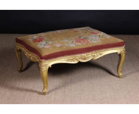 A Large Carved Giltwood Stool in the Louis XV Style. The generous serpentine edged rectangular seat covered in woolwork tapes