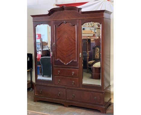 CIRCA 1900 MAHOGANY COMBINATION WARDROBE having a shaped top cornice over twin outer bevelled edge mirrored doors and central