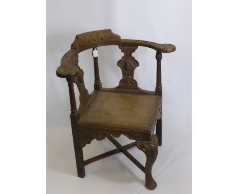 An Antique Oak Corner Seat, with decorative carving to the arm rests and back panel, cross stretchers.