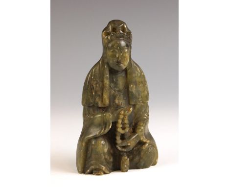 A Chinese carved green soapstone model of Guanyin, 19th century, modelled seated holding a string of beads, 12.5cm high