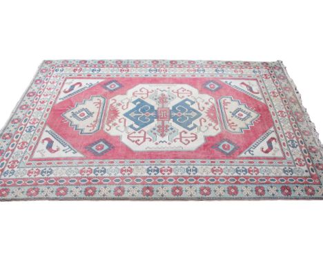 A hand woven Turkish village wool rug, in dark pink, green, light blue and ivory colourways, the central red field with a geo