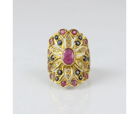 A yellow metal ruby, sapphire and diamond dress ring, possibly Thai, the central oval ruby within a flower head designed moti