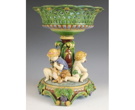 A Mintons majolica tazza, 19th century, modelled as a pierced basket raised above three putti representing hunting, fishing a