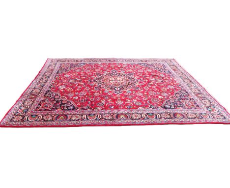 A rich red ground full pile Persian Mashad carpet, in red, blue, green and ivory colourways, the central foliate ogee shaped 