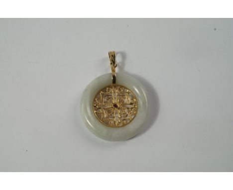 A 15ct gold and jade pendant, the ring of white jade centred with filigree gold work and a single ruby, approx 3.3cm wide. CO