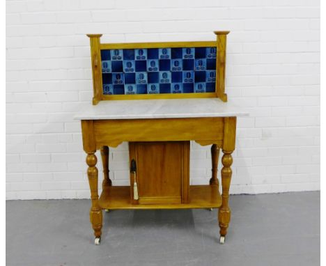 A pine ledgeback wash stand with a blue tiled splash back over a marble rectangular top with a cupboard to the undertier on t