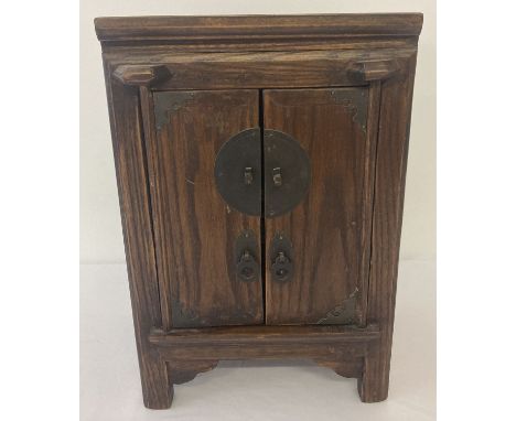 A dark wood small table top oriental style 2 door cabinet. With interior shelf and small drawer. Metal drop handles and door 