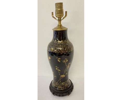 A black ceramic table lamp base with painted gold floral detail. On a carved wooden base. Approx. 44cm tall (to include base 