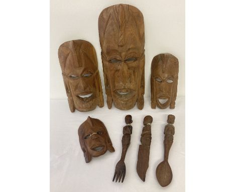 A collection of African carved wooden tribal items. Comprising 4 Kenyan masks of varying sizes and a matching knife, fork and