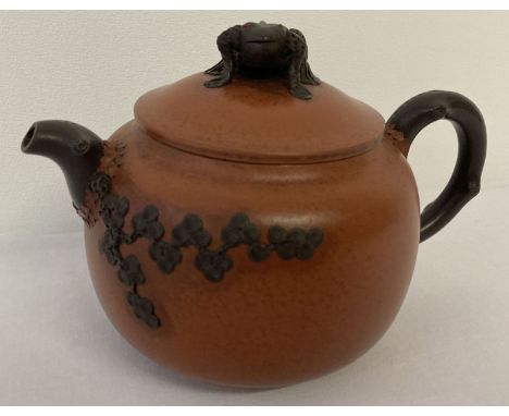 A brown and orange glaze terracotta teapot with cherry blossom detail and frog shaped finial to lid.  Approx. 9cm tall.