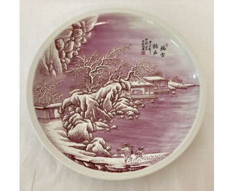 A signed, hand painted pink and white ceramic plate depicting a snow scene.  Approx. 30.5cm diameter.