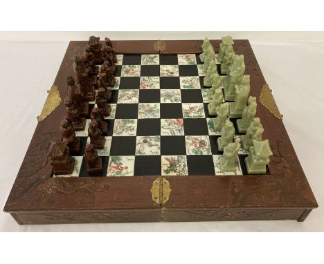 A wooden cased oriental design chess set with brass hinges, plates and handles. Carved dragon, bat and phoenix detail to body