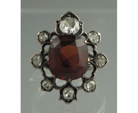 A VICTORIAN HESSIONITE GARNET AND DIAMOND CLUSTER RING, the central cushion cut garnet surrounded by old cut diamonds. Ring s
