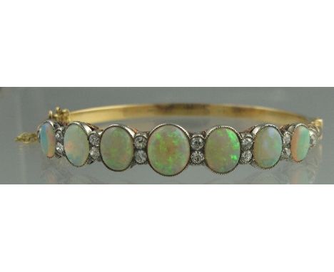 AN EDWARDIAN OPAL AND DIAMOND OVAL HINGED BANGLE, the seven graduated oval opals separated by pairs of old cut diamonds with 