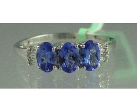 AN 18CT WHITE GOLD TANZANITE AND DIAMOND RING. The three oval tanzanite stones an estimated 6mm x 4mm, having four baguette c