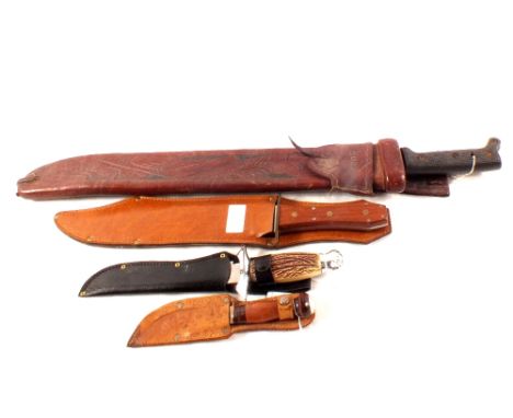 A machete with leather scabbard marked Cuba, with a John Wayne commemorative bowie and two sheath knives