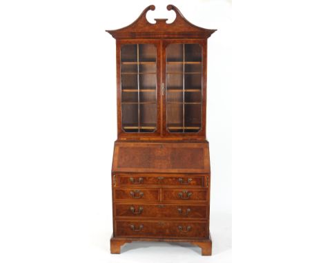 A reproduction mahogany and burr wood bureau bookcase, the broken swan neck pediment above glazed panel doors enclosing shelv