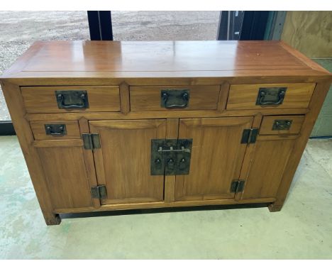 An Oriental style hardwood solid sideboard with large metal handles and iron plates with five drawers above cupboards with sh