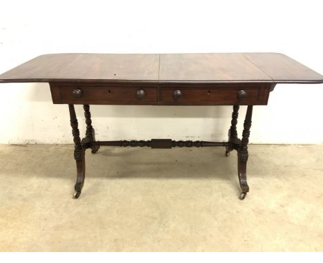 A Regency style mahogany sofa table on brass castors with turned stretchers, two drawers with dummy drawers to the other side