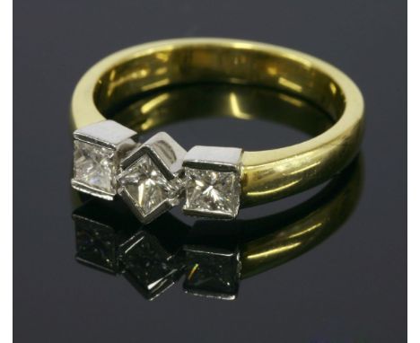 An 18ct yellow and white gold three stone princess cut diamond ring, a central princess cut diamond partially rub set in an o