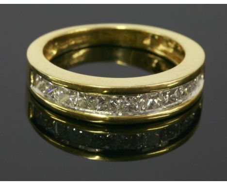 An 18ct diamond set half eternity ring, with a row of slightly graduated princess cut diamonds, channel set to raised guards,