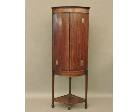 A mahogany bow front and box wood strung corner cupboard, on a stand, 189cm high