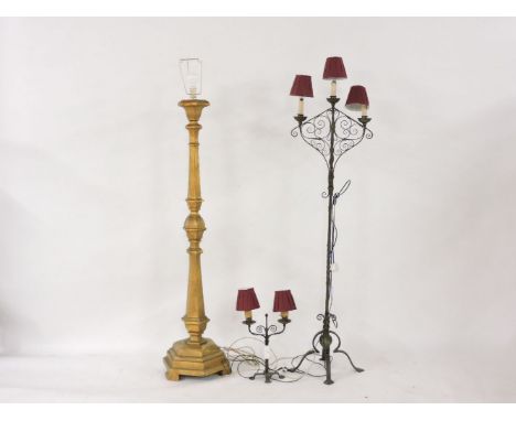 A gilt standard lamp, in the Baroque style, a wrought iron three light standard lamp, and a table lamp