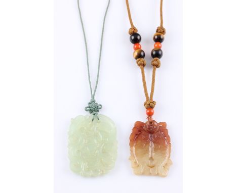 Two oriental hardstone carved pendants, one being green in colour and having foliage design, suspended from a green cord, the