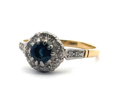A Sapphire and diamond cluster ring, stamped 18ct. Size P. Weight 3.24g. Sapphire 5mm in diameter and with teal hue.