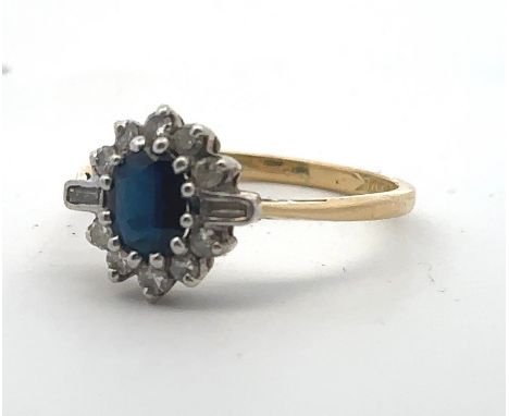 An 18ct gold, sapphire and diamond cluster ring. Central oval sapphire surrounded by baguette and round brilliant cut diamond
