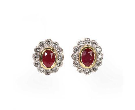 A pair of ruby and diamond cluster stud earrings, each with a central oval cut ruby, bezel set to a surround of round brillia