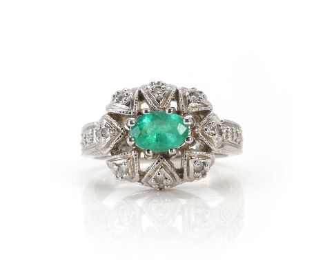 A 14ct white gold emerald and diamond ring,  a central oval cut emerald, 7mm x 5mm, claw set to a high domed pierced head, gr