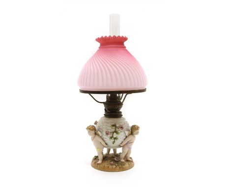 A porcelain three cherub oil lamp, with pink swirled glass shade.45cm high to top of chimney