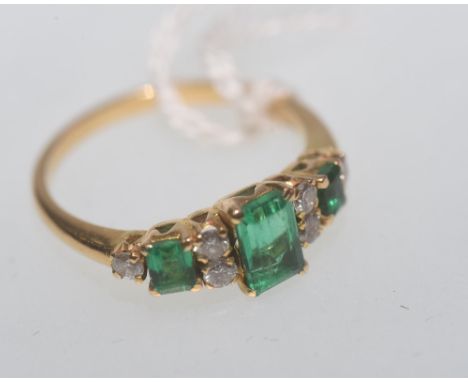 An emerald and diamond ring, the three graduating rectangular step-cut emeralds, each four claw set and spaced by pairs of br