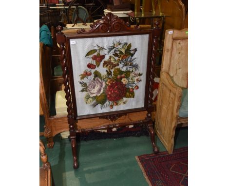 A late 19th century mahogany fire screen, the leaf and scroll carved pediment over a glazed needlework panel, flanked by bold